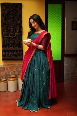 Women’s handloom half saree set in rich green and red tones, styled with a matching blouse and traditional South Indian silhouette.