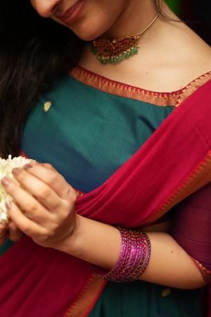 Close-up of the green half saree fabric and red pallu highlighting intricate handloom weaving and elegant ethnic detailing.